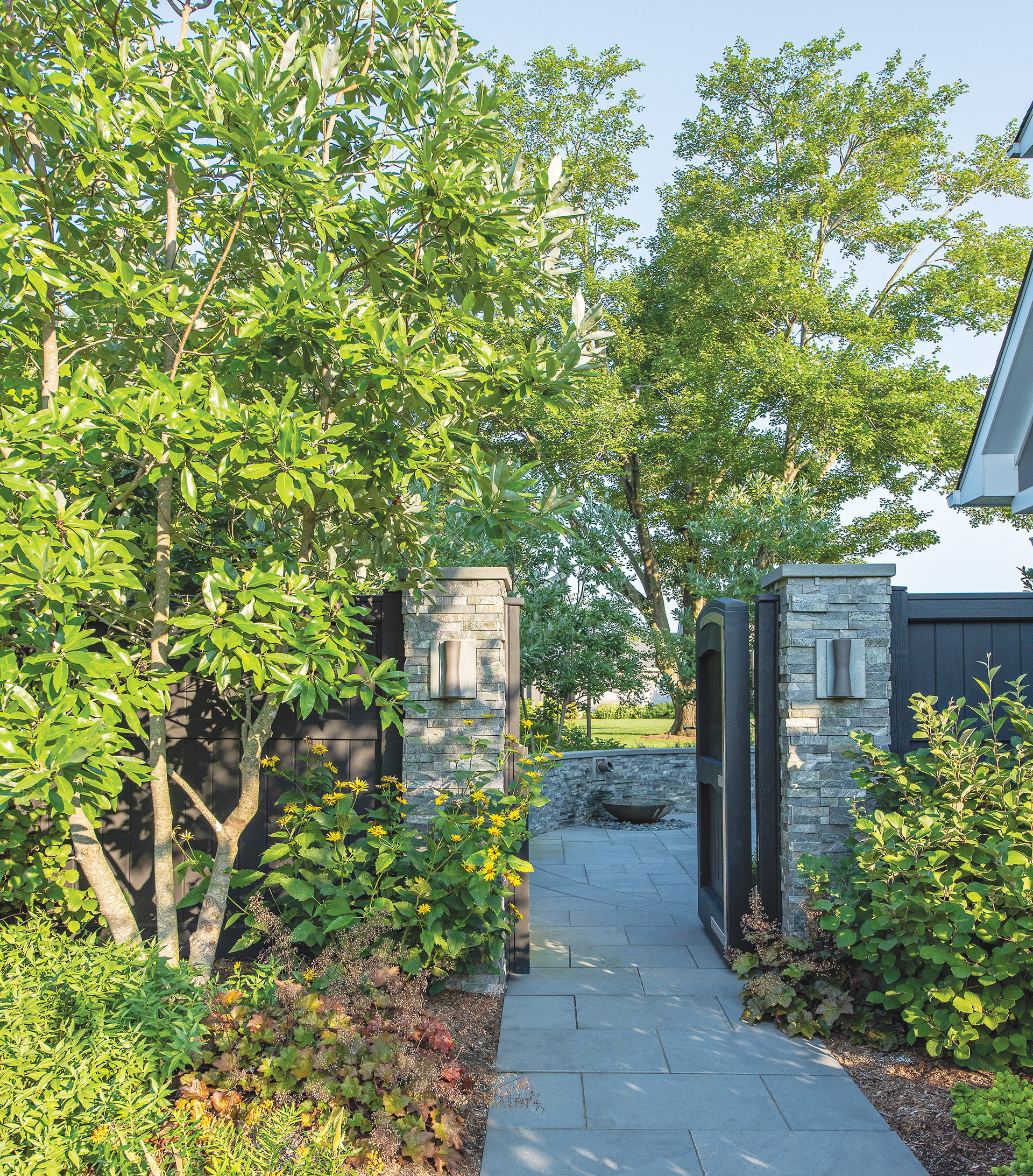 Black-stained garden gate, stone-rimmed courtyard, and concrete-and-copper water feature from Lunaform.