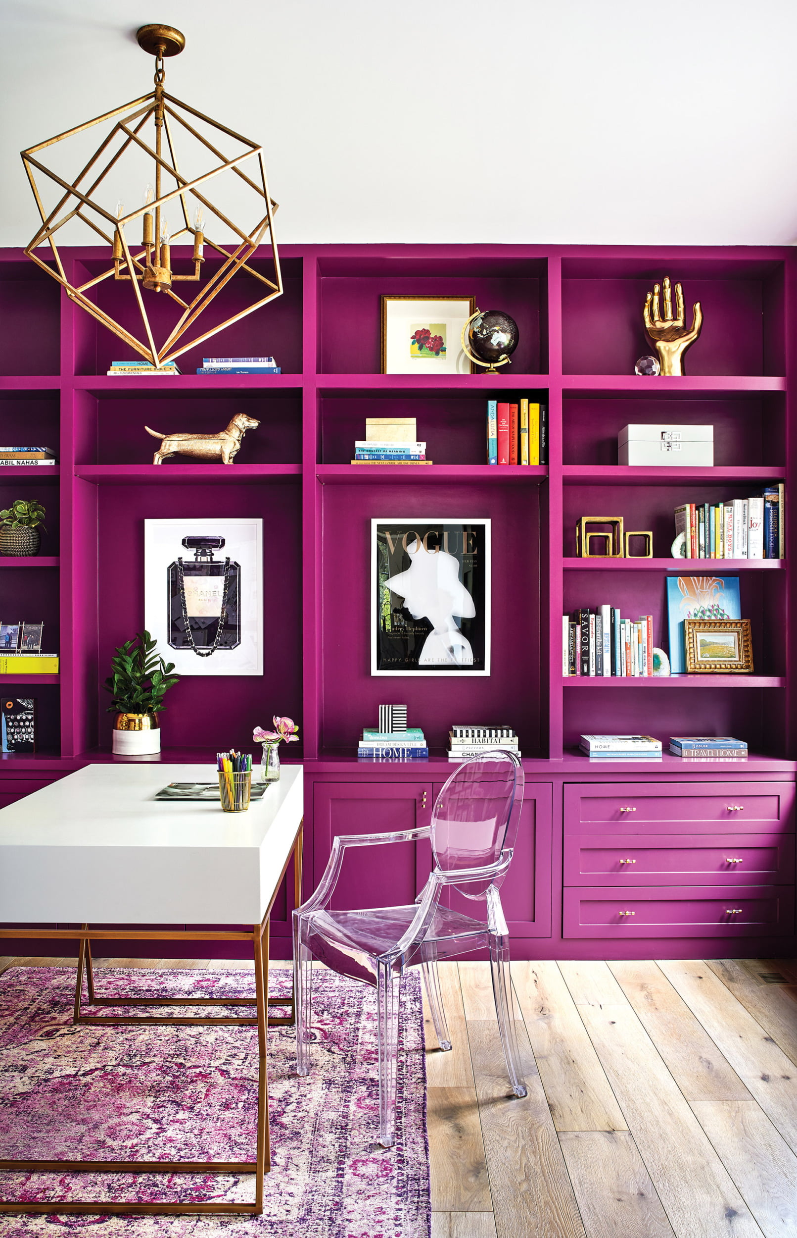 Bright-pink home office features chic writing desk and acrylic chair atop a colorful rug.