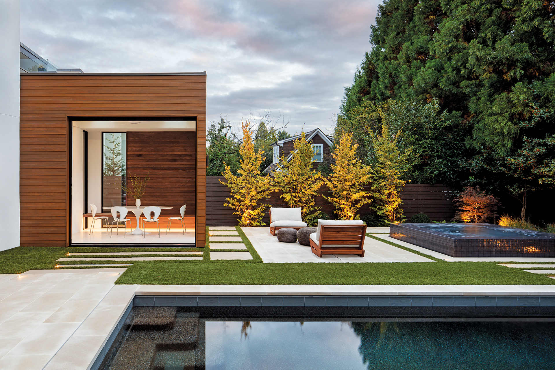 A breakfast room addition featuring ipe cladding and glass pocket doors by Western Window Systems. The pool area, designed by Fine Earth Landscape, includes buffed-limestone pavers and a black-granite infinity-edge spa