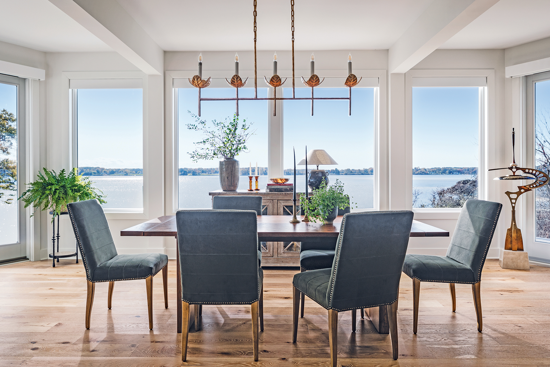 Elegant dining room with windows framing a watery view and automated roller shades | Home and Design Magazine