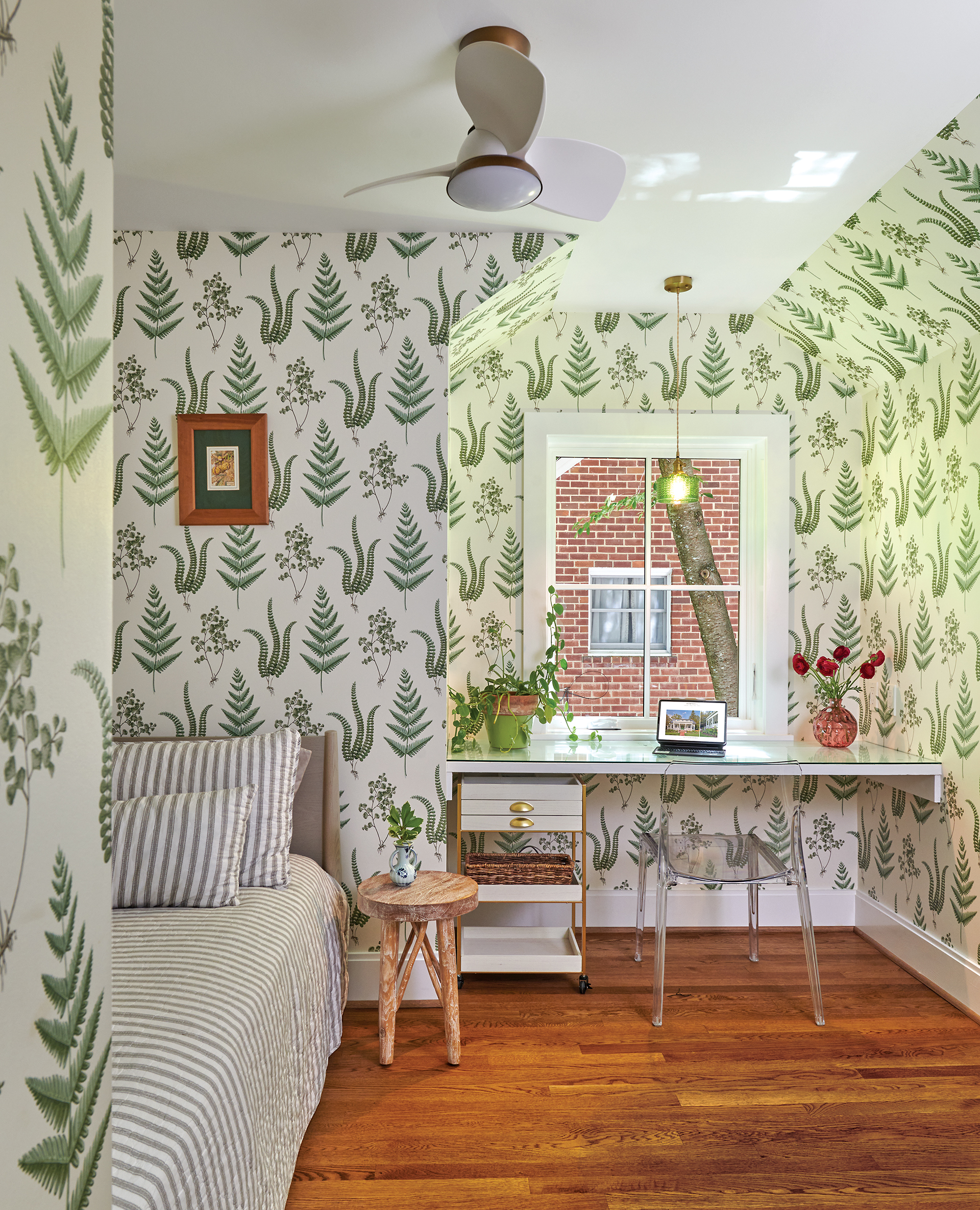 small bedroom that doubles as a home office with fern wallpaper and a ceiling fan